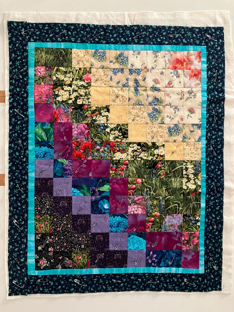 Quilt made of small squares with gradations of flowered fabric from dark in lower left to light in upper right corner