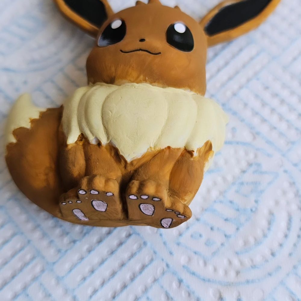 A painted statue of eevee, this time lying down. They have small paw pads that are crudely drawn on their paws