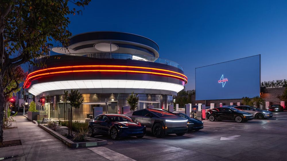 An image of the Tesla Diner in Los Angeles. It is a two-story silvery-gray building with a neon stripe around the first floor. 