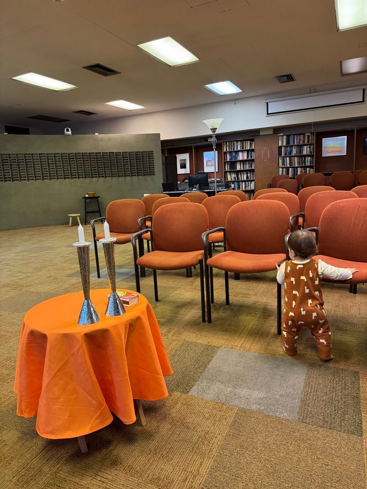 Photo shows a baby in llama overalls next to a table with Shabbat candles 