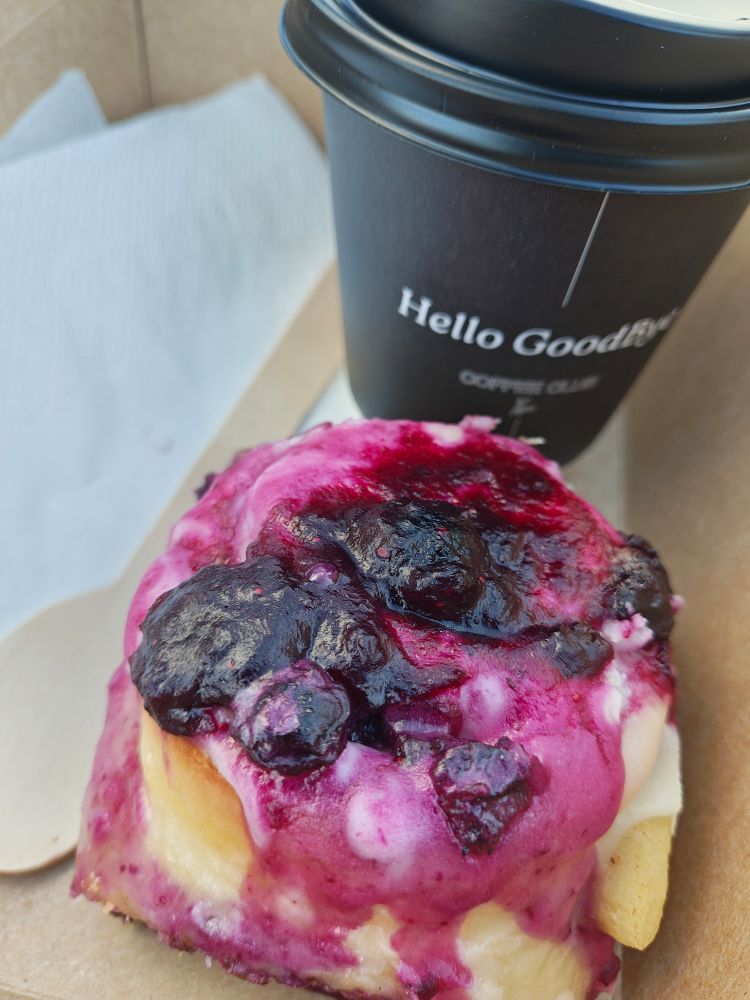 A picture of a coffee cup and blueberry topped cinnamon roll.