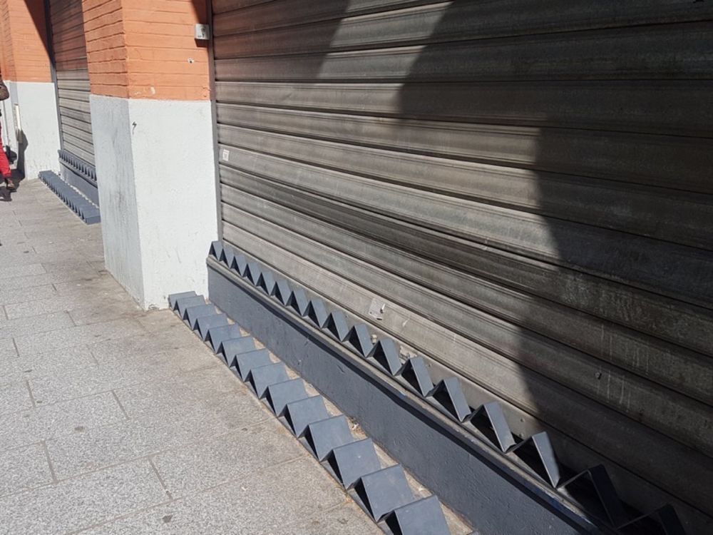 Two rows of triangle angled metal along sidewalk and building side