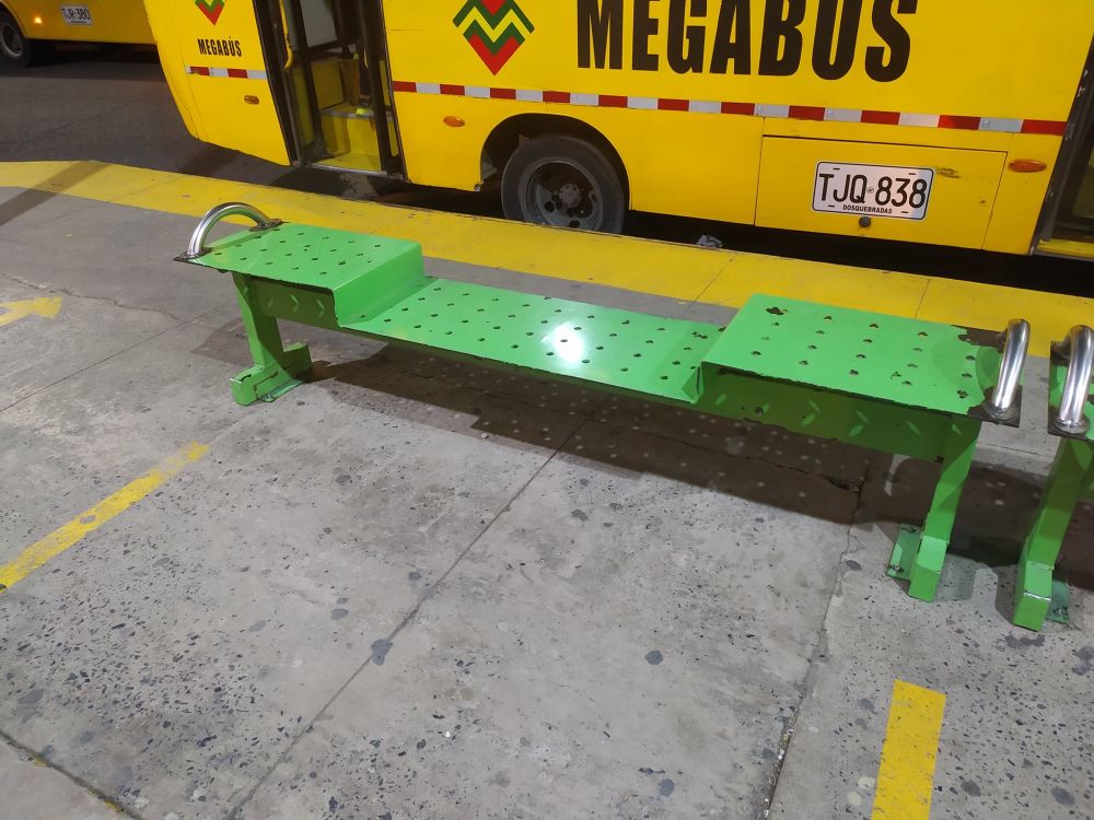 A neon green bench on a sidewalk in front of a yellow bus. The center portion of the bench is lower than the ends.