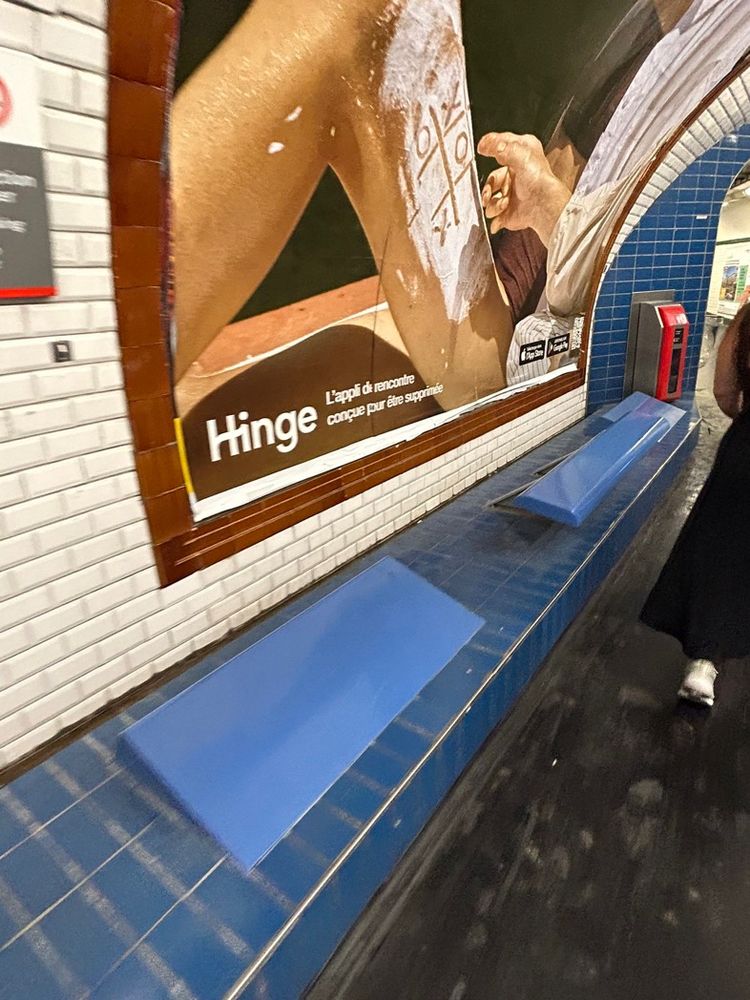 A blue tiled bench in a metro station with additional panels raised and tilted to make it uncomfortable