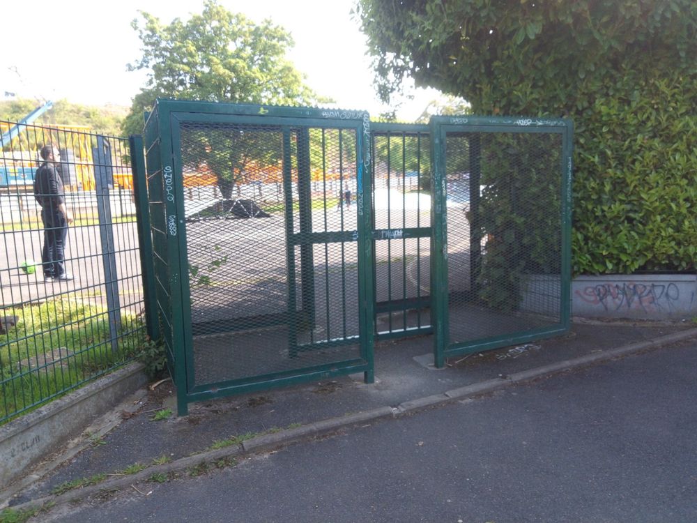 Green gate entrance to a playground with a narrow, zigzag opening