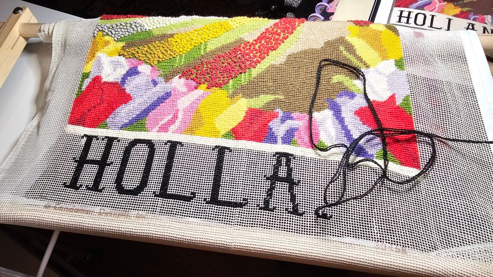 Work-in-progress snapshot of a needlepoint canvas with colorful tulips and the letters "HOLLA" (the last "ND" not stitched yet) from 1980's craft kit.