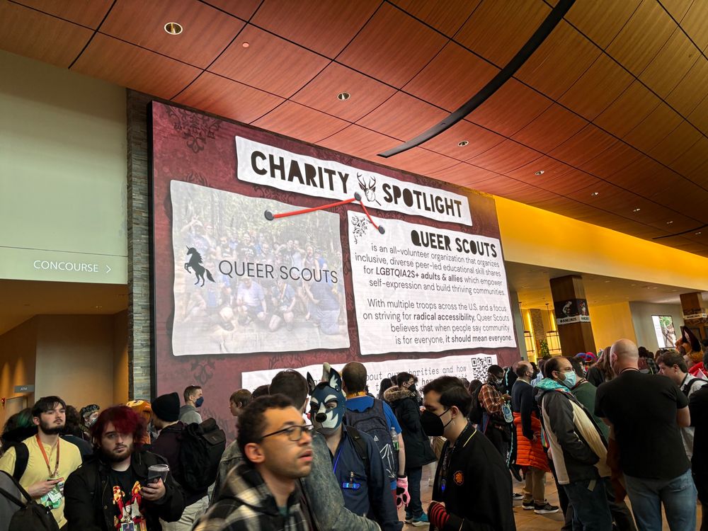 Image of a crowded room with a large screen highlighting queer scouts as one of anthro New England’s charities 