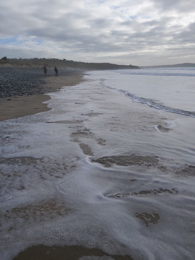 A grey sky  with waves lapping up the beach.
