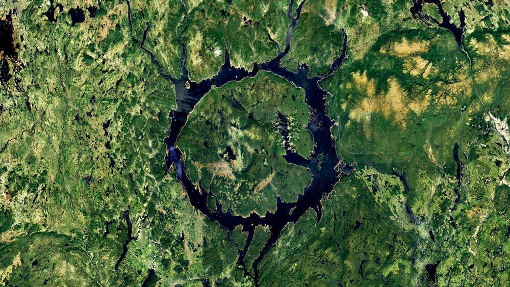 a satellite picture of a circular lake amidst a very green landscape. the lake has got a circular island in its middle, making the lake appear as a donut shape