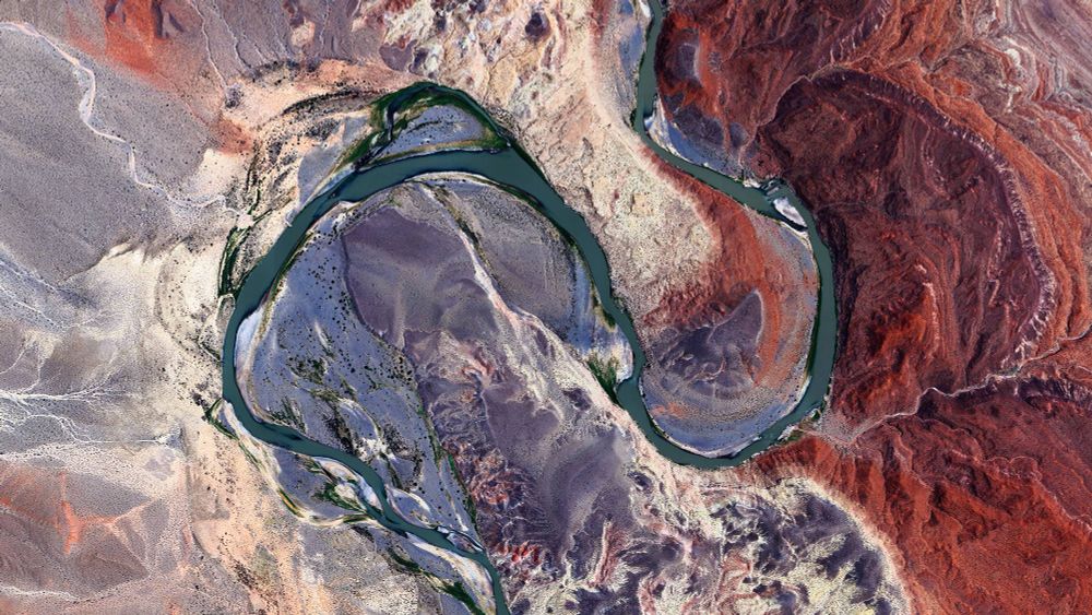 a river meander seen from above, all around is a desertic landscape in purple and red tones