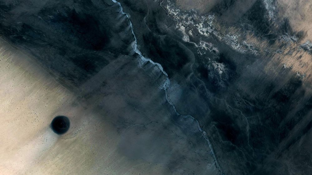 Sudan

a desertic landscape seen from above, in which a clear sandy zone melds into black sand. a black dot is present on the left side in the middle of the clear sand, giving it an abstract painting quality