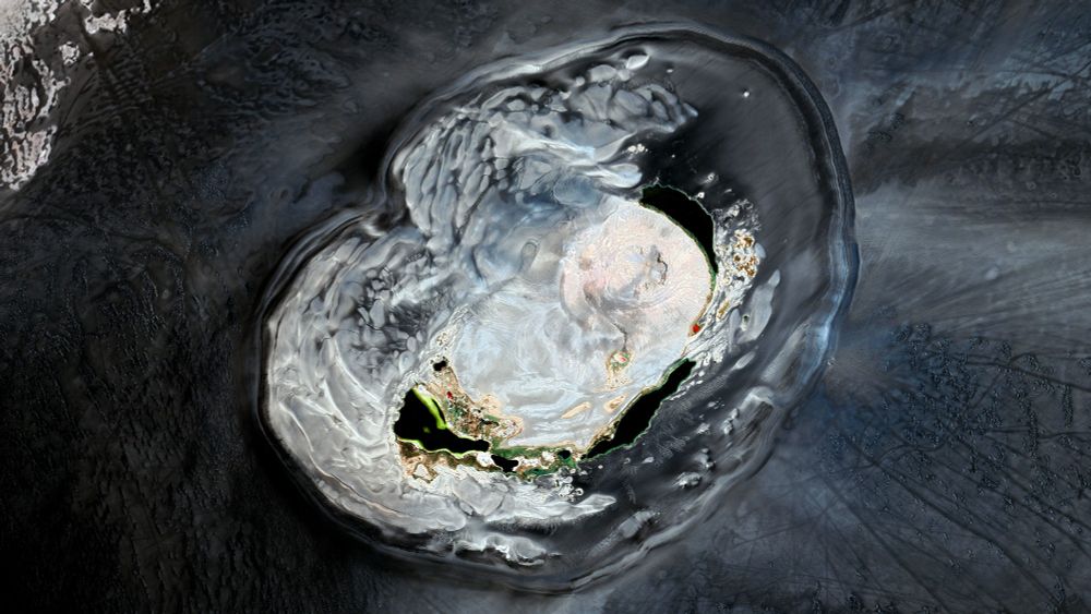 A satellite picture of a volcanic structure amidst black sand. The structure is clearer than its surroundings and we can see lakes and a crater in the middle of it.