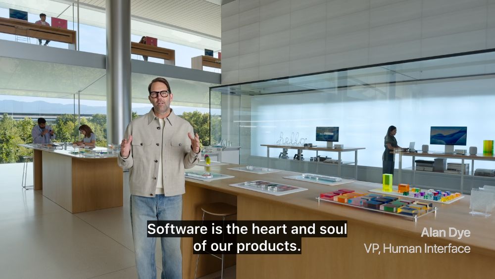 photo of a bleak looking hotel lobby-like room with coloured glass blocks on the table. Alan Dye, VP of Human Interface, a white man with thick black glasses stands with subtitle "Software is the heart and soul of our products"