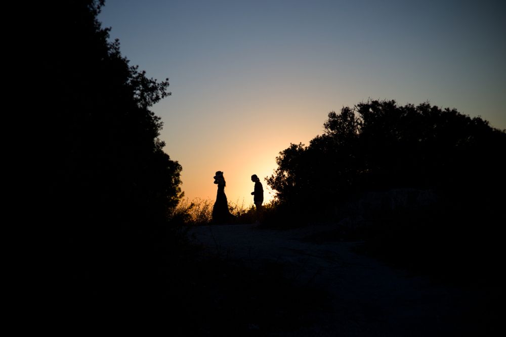 photo of clear sky with setting sunlight gradient from top blue to bright gold in centre frame. Silhouette of trees and bushes frames two figures in the centre