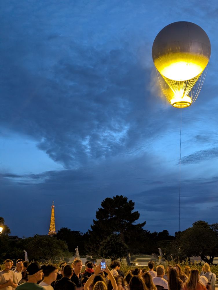 The olympic balloon aloft in Paris, the Eiffel tower lit behind it.