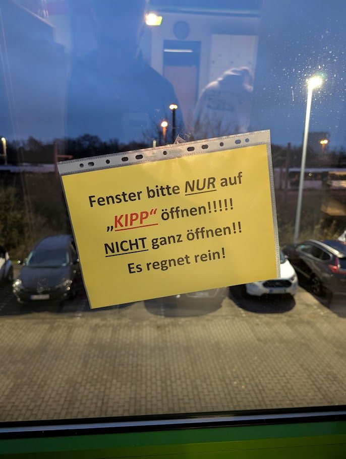Ein gelber Zettel in einer Klarsichtfolie wurde auf ein Fenster geklebt. Auf dem Zettel steht: Fenster bitte NUR auf "KIPP" öffnen!!!!! NICHT ganz öffnen!! Es regnet rein!