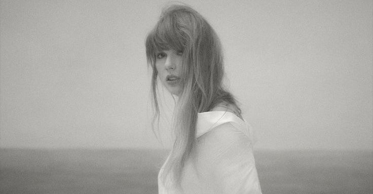 taylor in a white button up off the shoulders a bit. she is looking to the left at the camera facing left with her body as well.