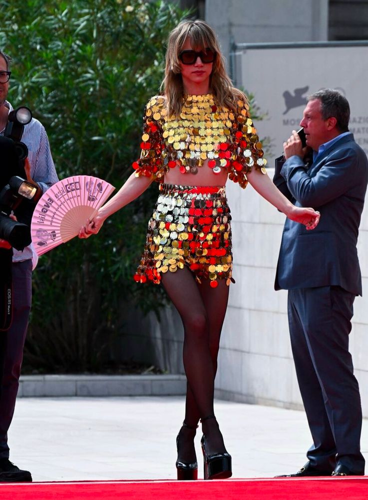 suki walking down a red carpet with her pink hand fan in her left hand. she is wearing the same outfit as previous pic. 