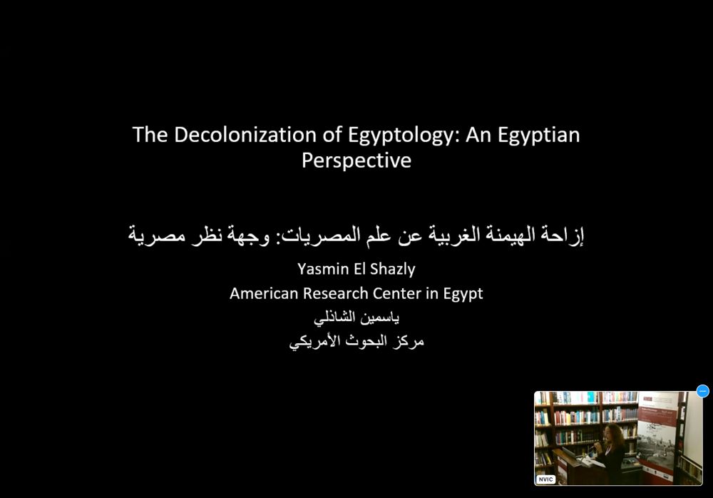 Screenshot of a PowerPoint slide entitled The Decolonization of Egyptology: An Egyptian
Perspective: Yasmin El Shazly with a small livestream window in the bottom right corner showing a woman at a lectern in a library 