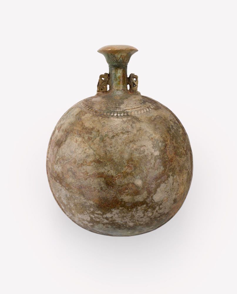 A mottled green lentoid-shaped flask with a neck shaped like a papyrus column flanked by miniature baboons, on a white background, dating to c600BC & on display at the National Museum of Scotland.
