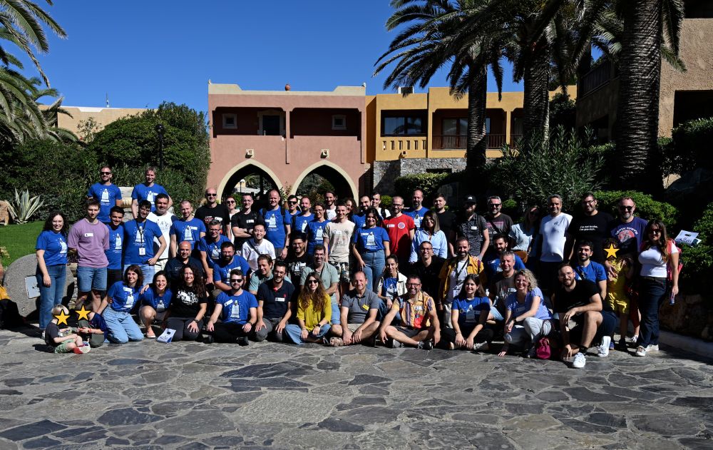 A group photo of all the participants which are around 50 with the hotel and palm trees as background in a sunny setting.