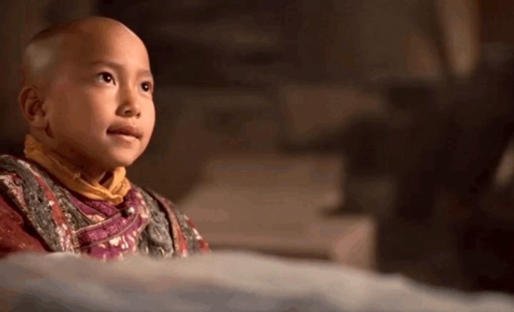 a young boy with a bald head is sitting on a bed and looking at something