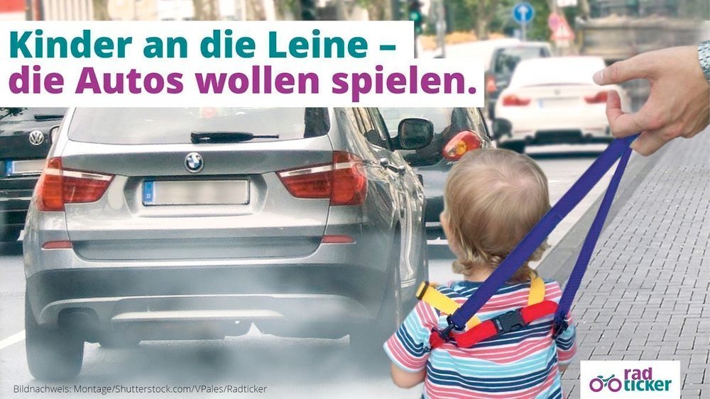 Ein Kleinkind steht an einer vielbefahrenen Straße. Es wird an einer Kinderleine von einem Erwachsen geführt. Text: Kinder an die Leine - die Autos wollen spielen.
