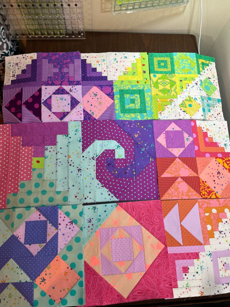 Quilt blocks in shades of blue, green, pink, and purple are arranged in the positions they will be assembled together 