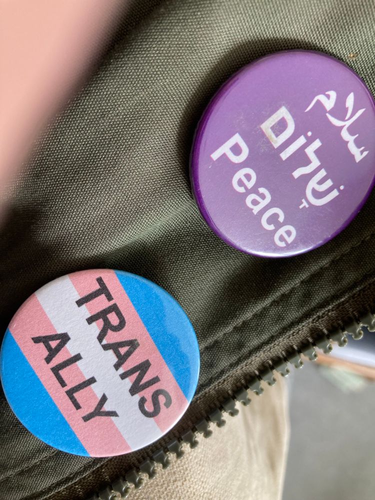 Two badges: one says Peace in English, Hebrew and Arabic (in support of Standing Together) and the other says simply “Trans Ally.”