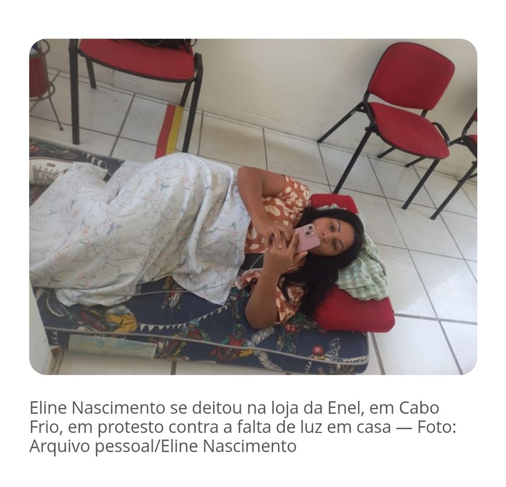 Print de jornal no qual mostra uma foto da diva Eline (ela ta de vestido laranja estampado de bolinha branca) deitada num colchonete coberta por um lençol enquanto mexe no seu celular rosa carregando