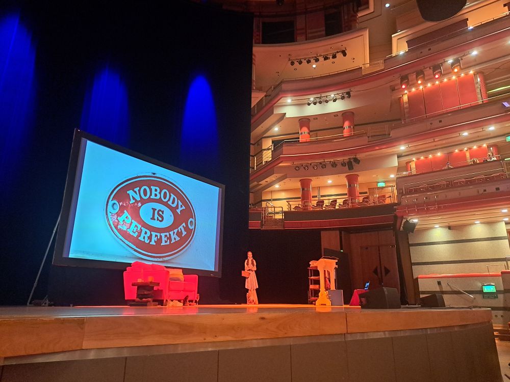 Stage at Birmingham Symphony Hall with a screen reading Nobody is Perfekt and a red sofa in front of it