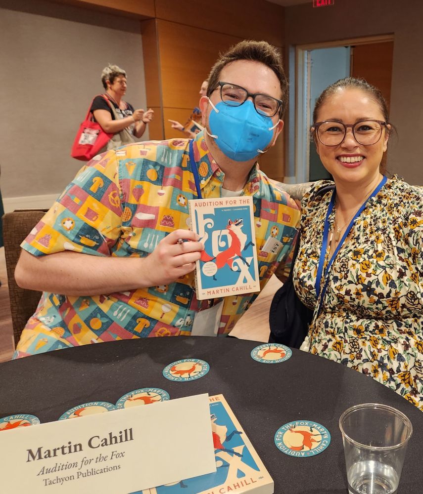 Marty, a man in a blue mask with a colorful shirt, posing with his friend Christine, a woman in a colorful dress and glasses