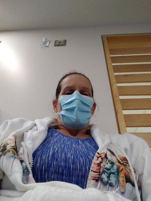 Selfie of @justbeingme_202 in the hospital waiting room before she was admitted.

She has her hair pulled back tight and is wearing a blue surgical mask, a blue and white striped top, and a cozy white zip up sweater with flowers across the front