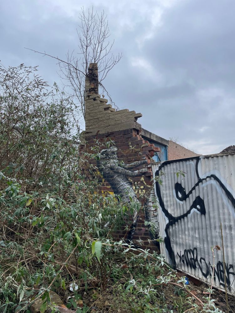 Half a brick wall with art by Phlegm, flanked by bushes and fences