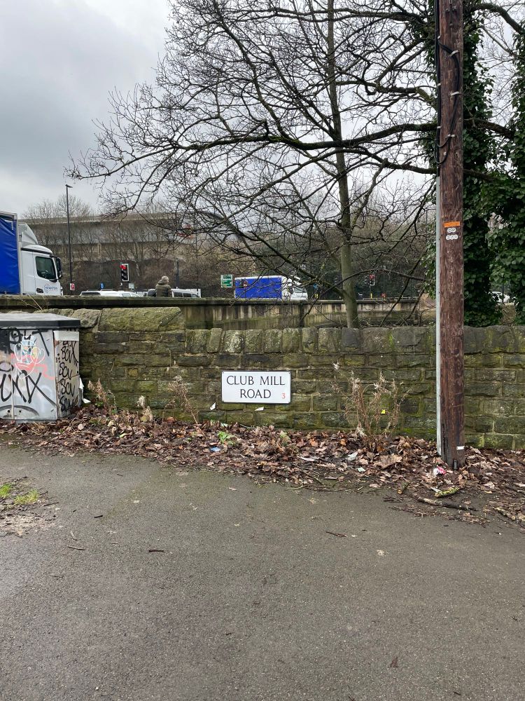 A sign reading Club Mill Road, path in foreground 
