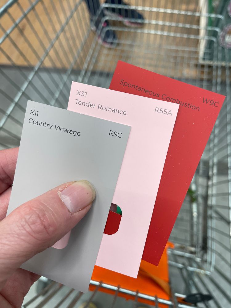 A hand holding three paint colour cards. In order; ‘Country Vicarage’, ‘Tender Romance’ and ‘Spontaneous Combustion’