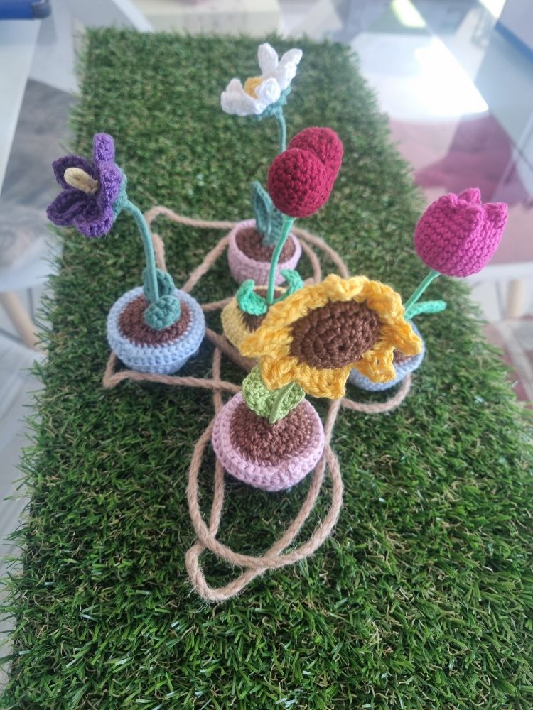 Auf dem Bild sieht man einen Tischläufer aus Kunstrasen und darauf fünf gehäkelte Blumen.