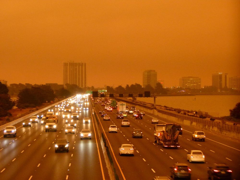 a freeway jammed with cars, headlights on, under a dark orange sky