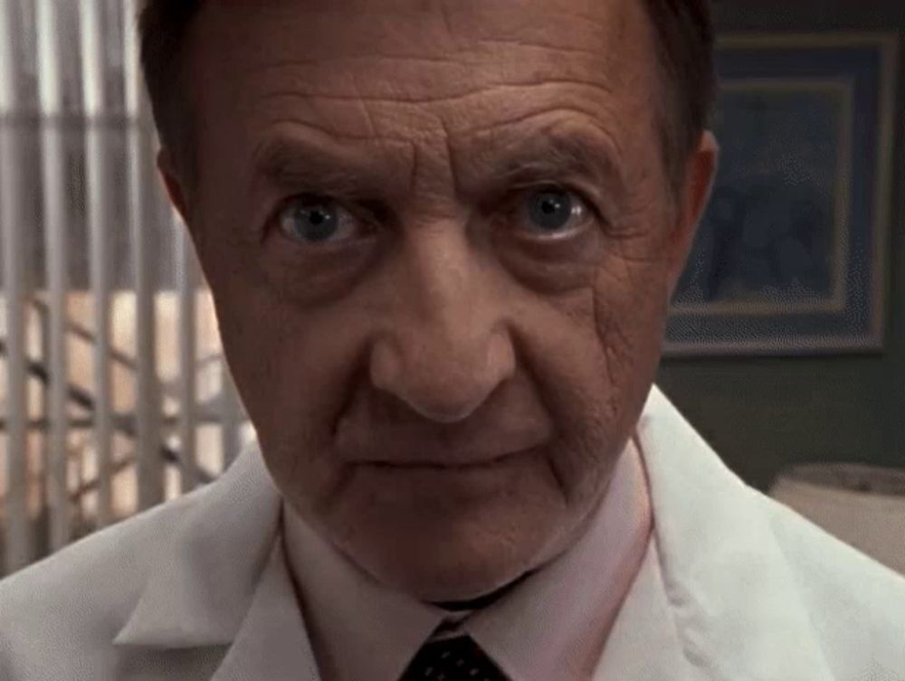 a close up of a man 's face with a white lab coat and tie