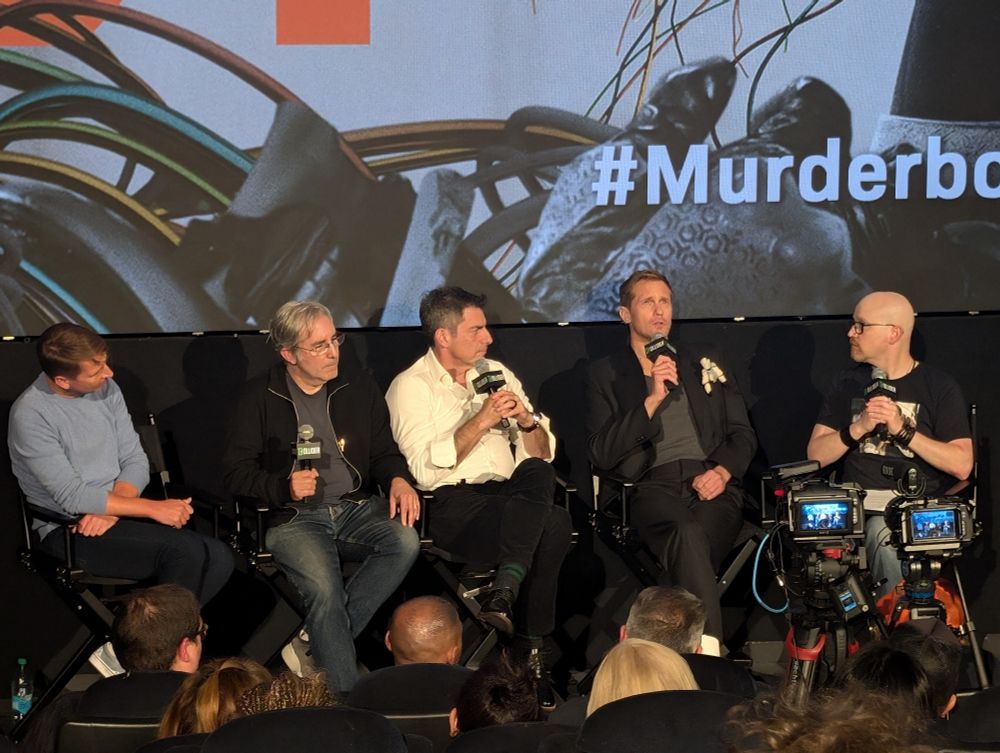 A zoomed in shot of a theater screen showing the title art for the AppleTV show Murderbot with 4 people sitting in front. The two show runners, the lead actor, and another actor from the show.