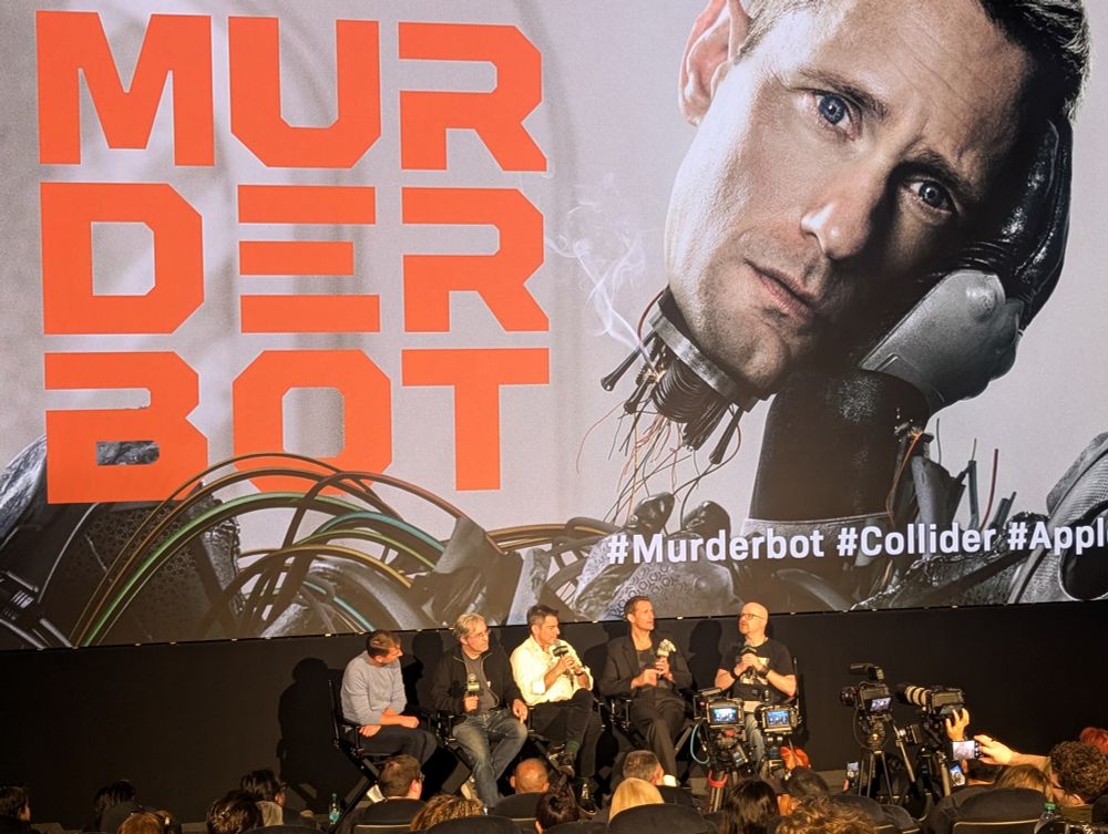 A theater screen showing the title art for the AppleTV show Murderbot with 4 people sitting in front. The two show runners, the lead actor, and another actor from the show.