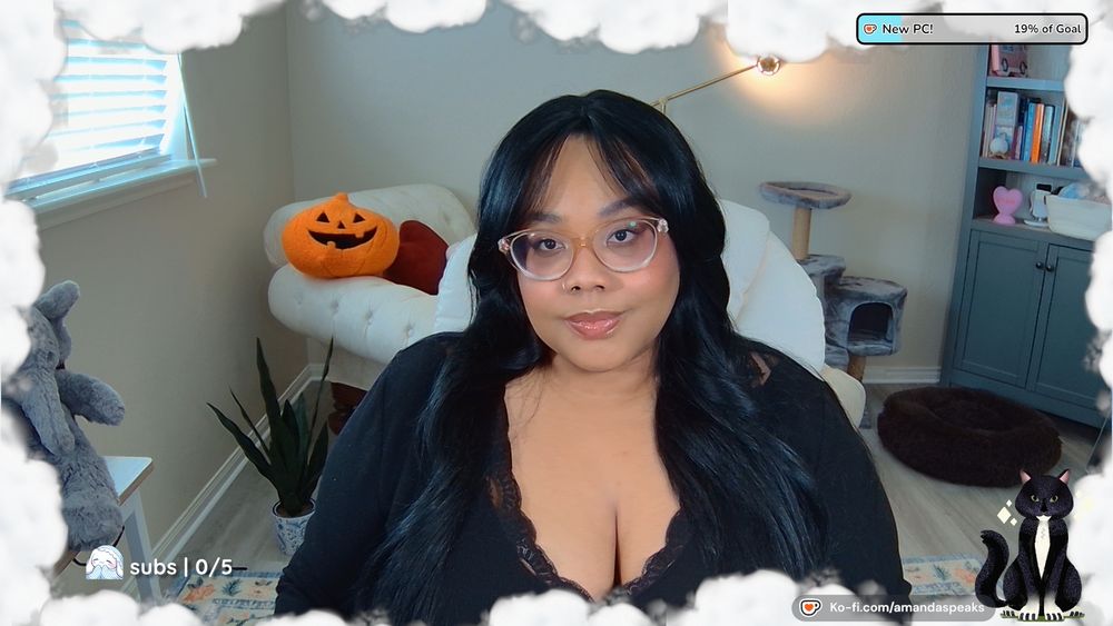 An image of Amanda; a Black person with long black hair and curtain bang. They are wearing a black long sleeved v-neck top and sheer gold framed glasses.