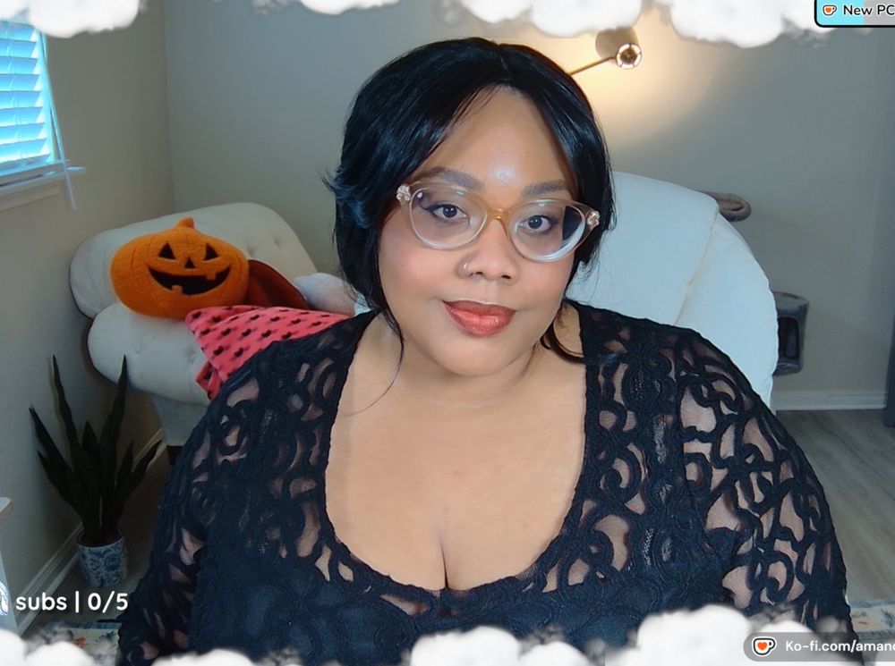 An image of Amanda; a Black person with black hair and curtain bangs in an updo. They are wearing a sheer black lacy patterned dress