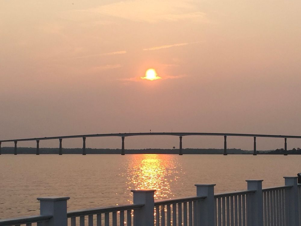 As the sun prepares to set over a bridge across a river, the water greets the sun with thousands of beads of light scattered between its ripples