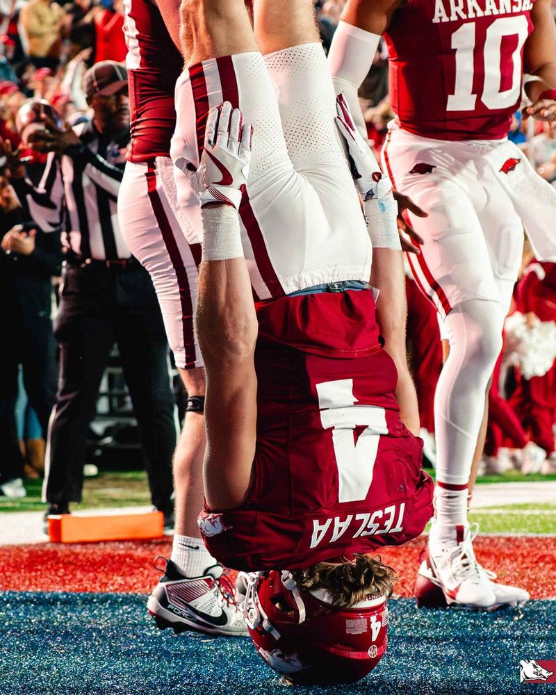 Issac Teslaa standing on his head in a football uniform in the endzone.
