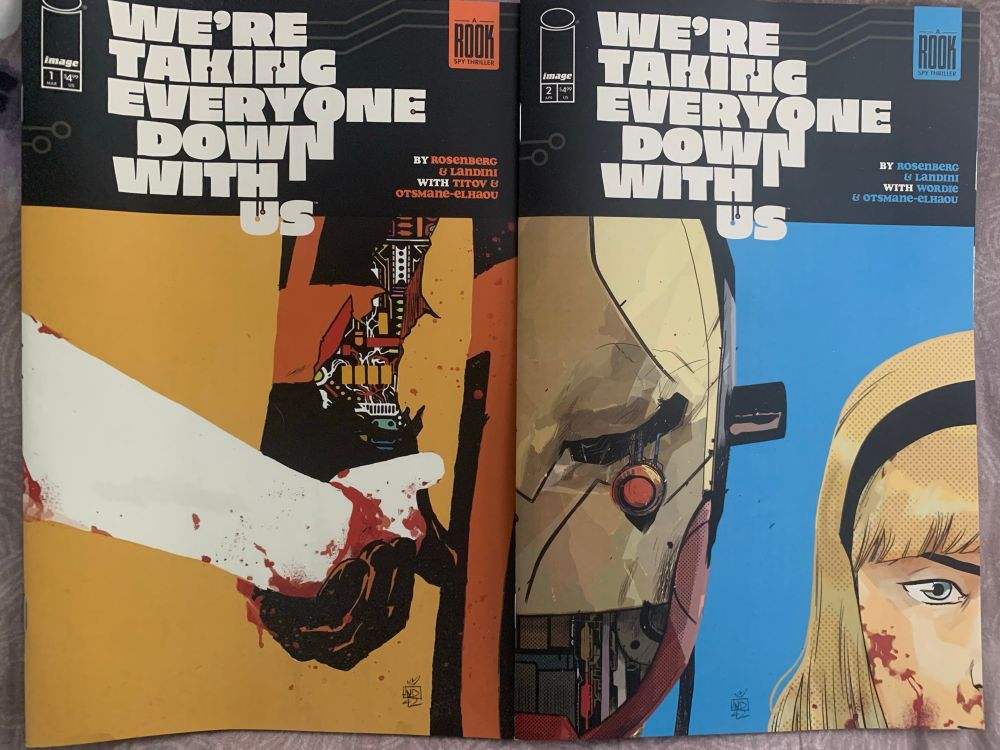 Photo of the covers of issues 1 and 2 of “We’re taking everyone down with us” comic book from Image.  First image is a girl’s hand in a banged-up robot’s hand, as if the robot is the parent.  Second image is a broken robot’s half face, and a girl’s half face.
Title font looks like a cool 70’s style.  Credits to Rosenberg & Landini, with Titov & Otsmane-Elhaou, also indicated as “A ROOK Spy Thriller.”