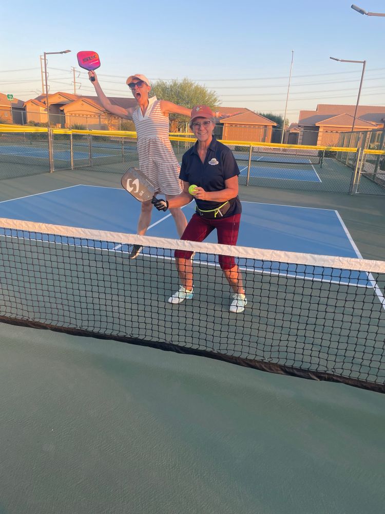 Two women posing with pickleball racquets with once jumping.