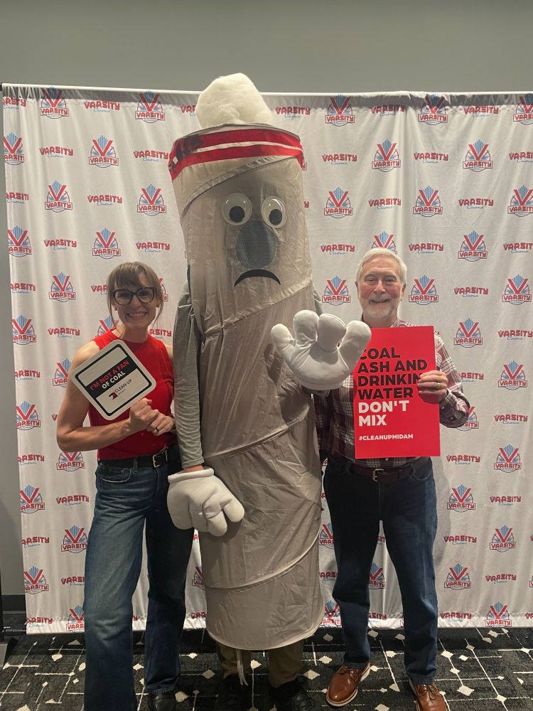 Two adults smiling posing with a human wearing a coal stack costume.