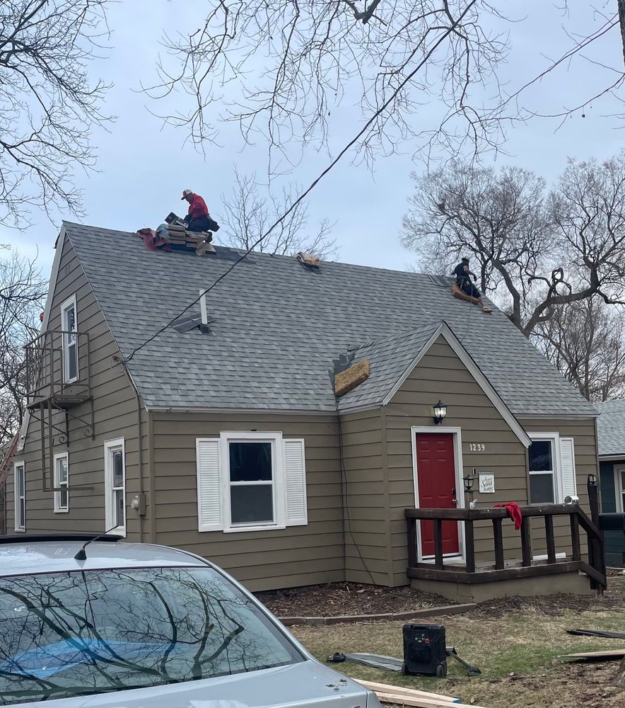 Roofers laying light gray shingles on a house.
