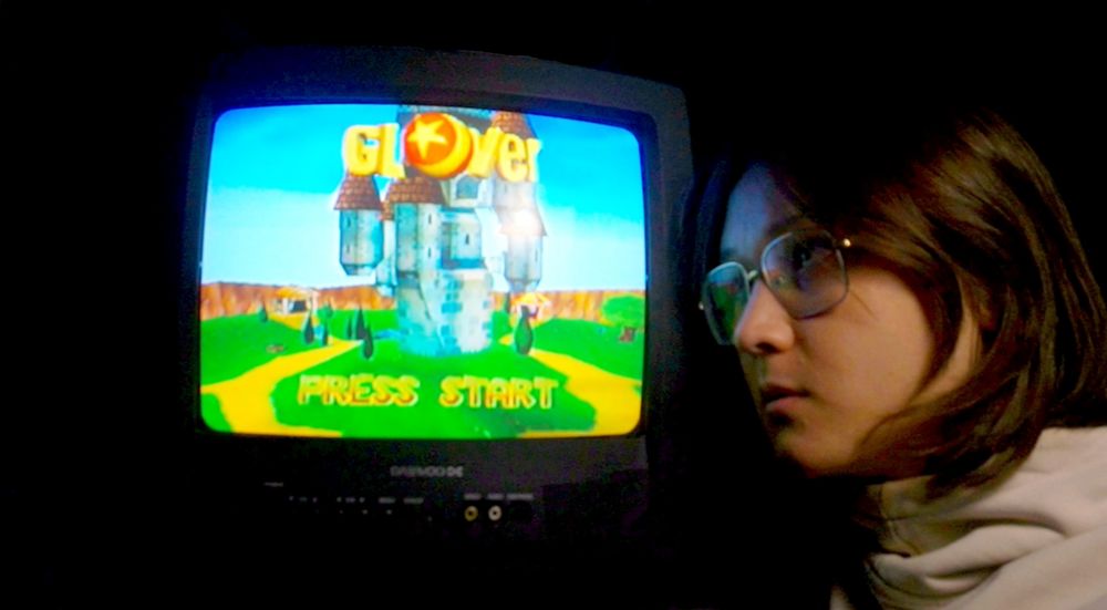 Harper stares at an old TV in dim light. The title screen for "Glover" is displayed on the TV
